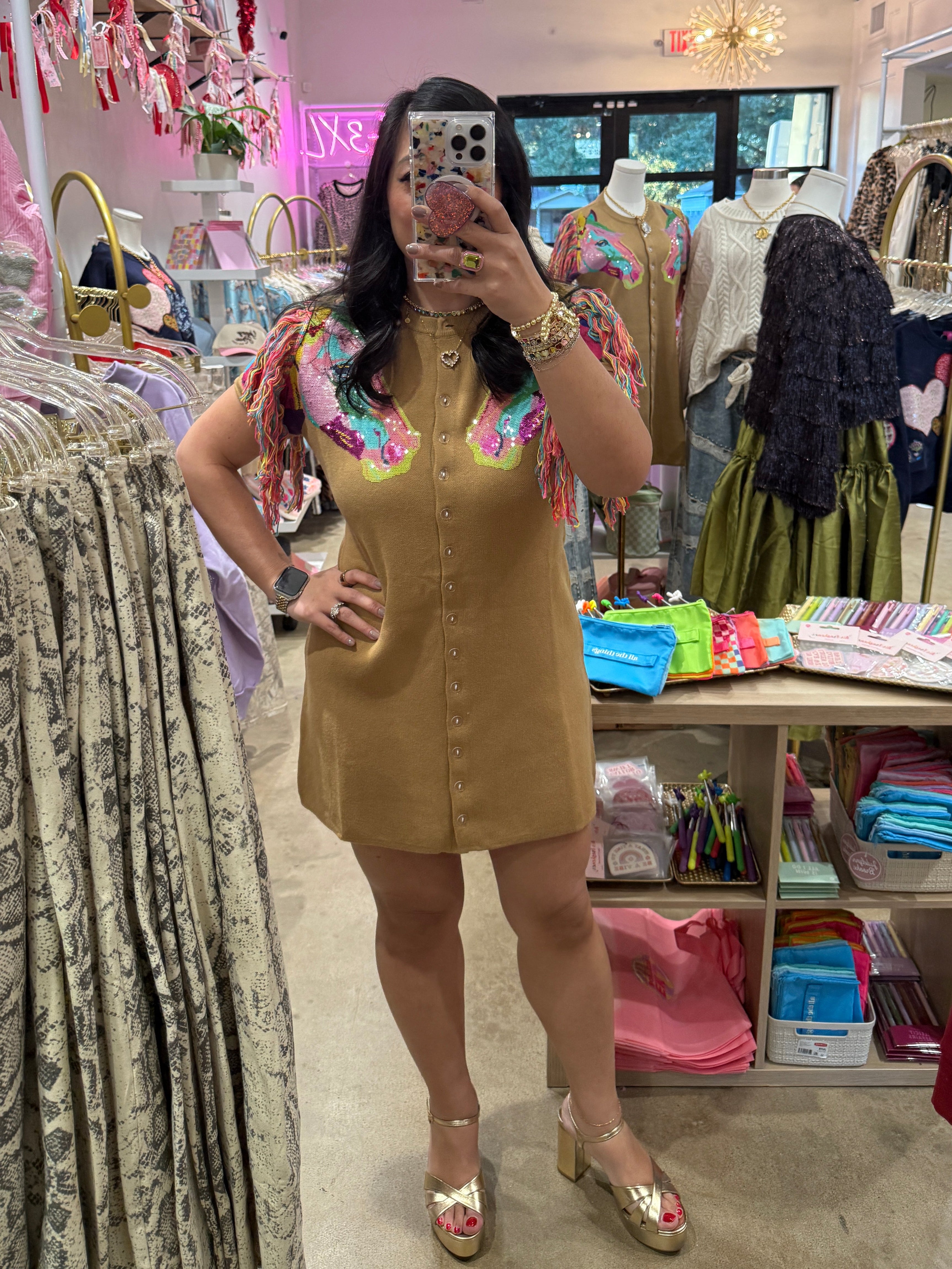 Woman taking a mirror selfie in a clothing store with various garments on display.