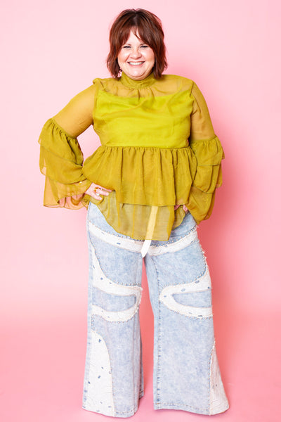 Woman wearing a green blouse and light blue jeans with lace details against a pink background