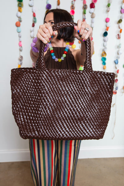 Brown braided tote bag held up by its handles in front of a colorful beaded backdrop