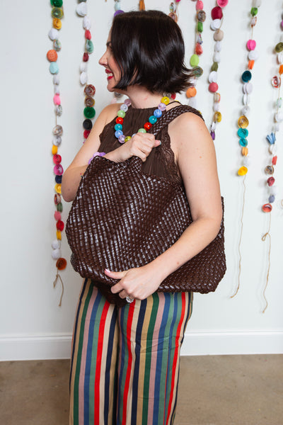 Side view of the brown braided tote carried on the shoulder in a boutique setting