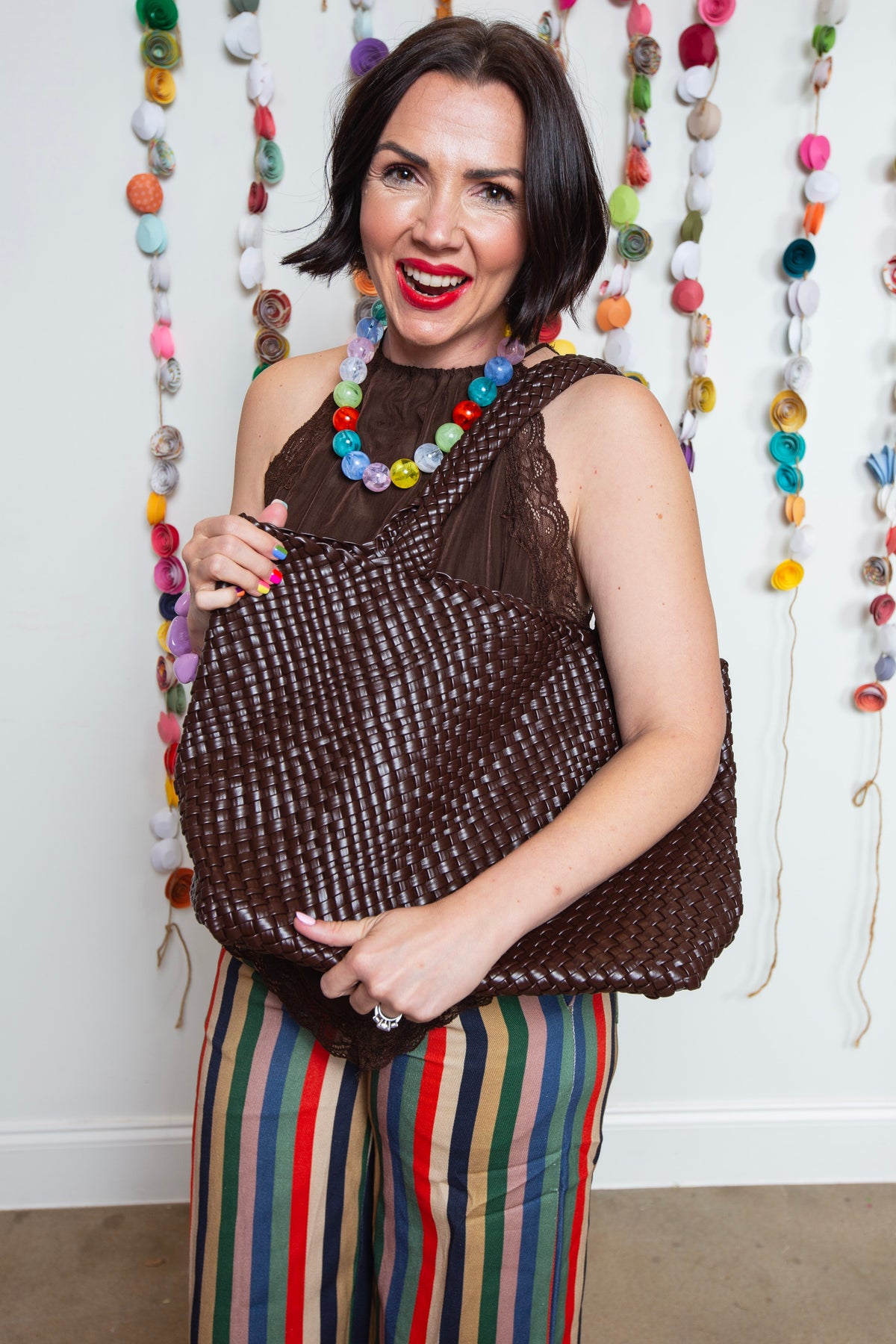 Brown woven tote carried on the shoulder with a brown top and striped pants