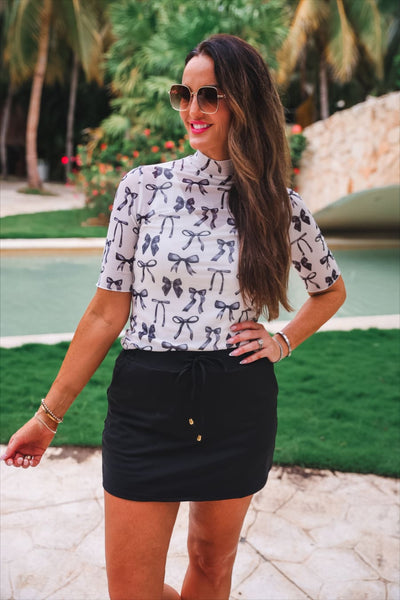 Black drawstring skort paired with a bow print mock neck top by a pool